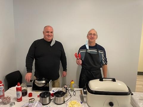 Two men smile while making waffles